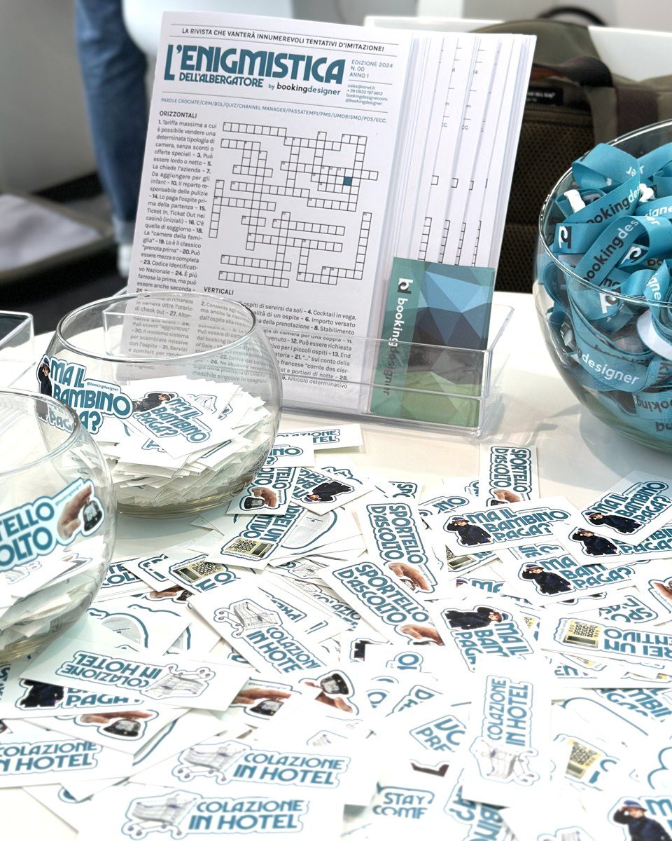 Il tavolo dello stand Booking Designer al TTG 2024 con L’Enigmistica dell’albergatore, gli adesivi e i laccetti